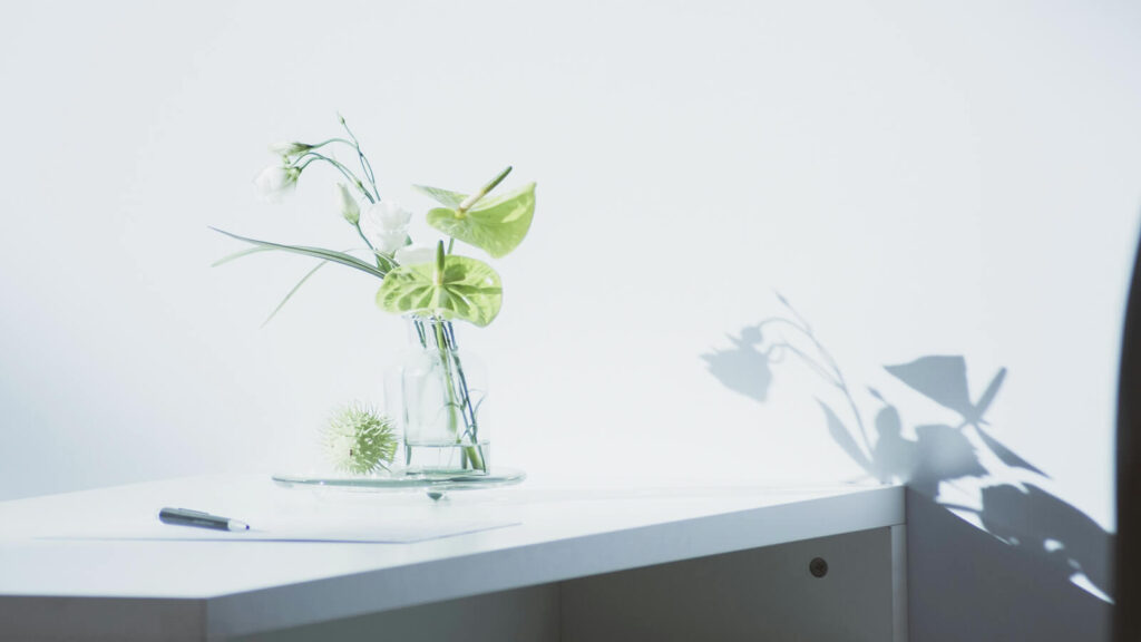 自然光に照らされたデスクと花。余白を生かした落ち着いたミニマルデザインの風景