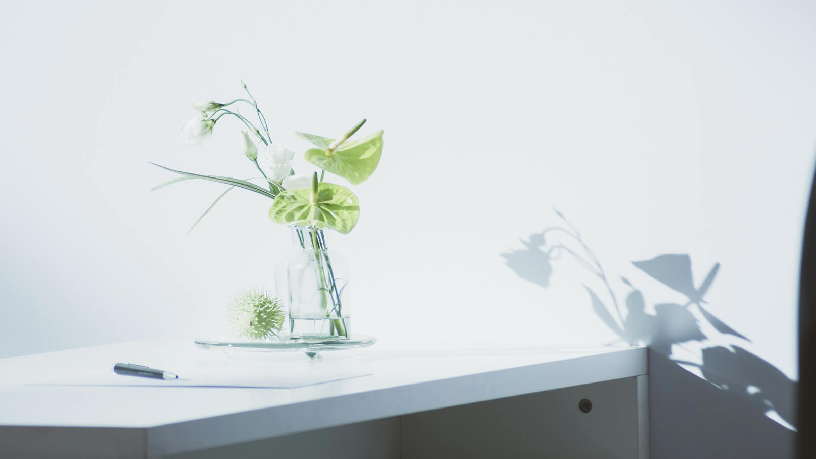 自然光に照らされたデスクと花。余白を生かした落ち着いたミニマルデザインの風景